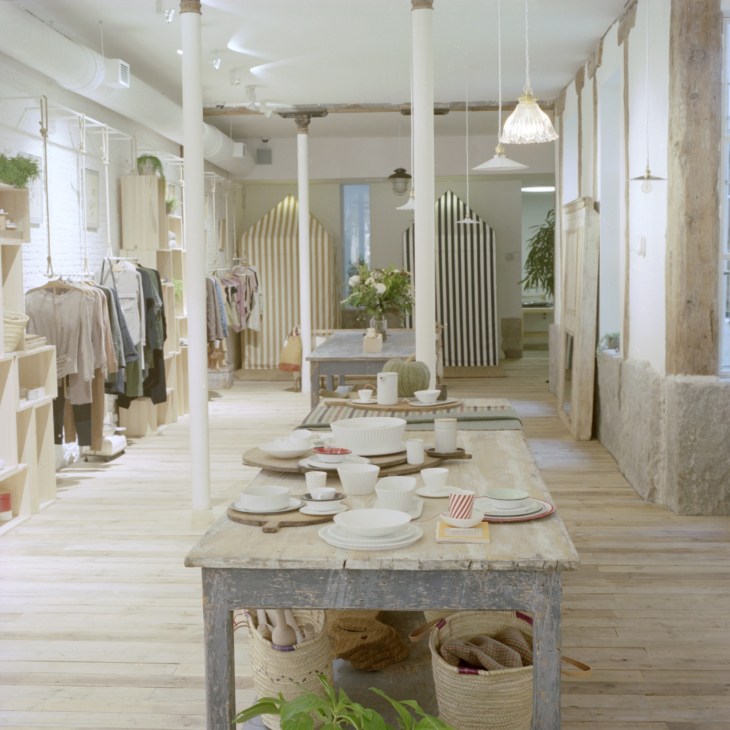 Interior of Do concept store in Madrid showing long wooden table with tableware, clothing racks, and minimalist design.