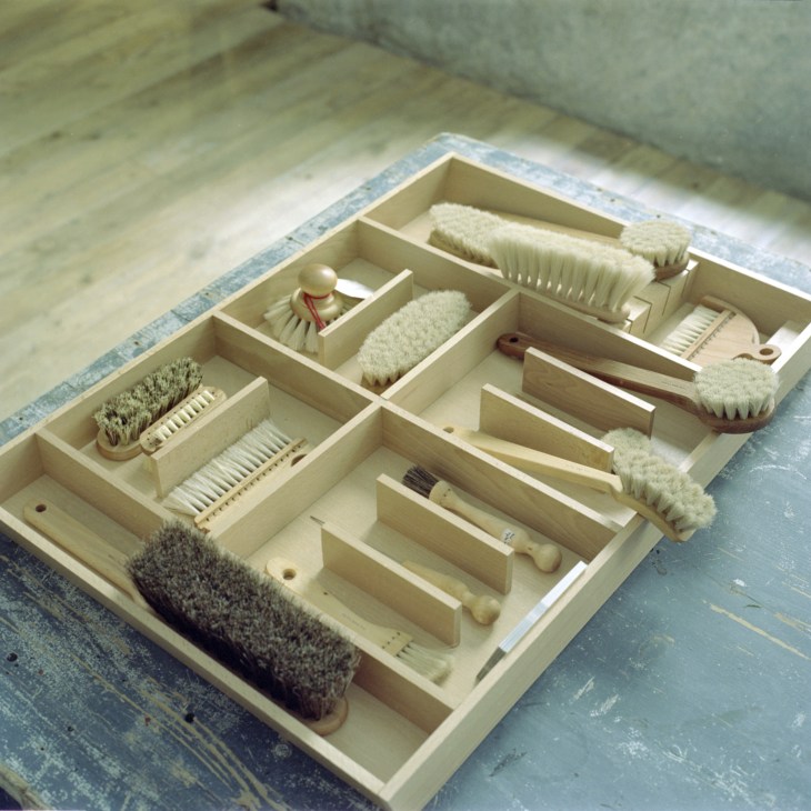 Organized drawer containing various brushes and cleaning tools in compartments.