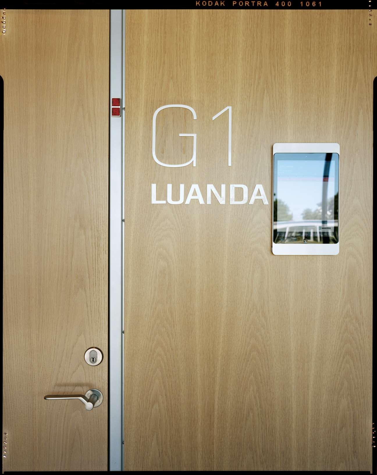 Wood-panelled door marked 'G1 LUANDA' with a small window showing an interior view.