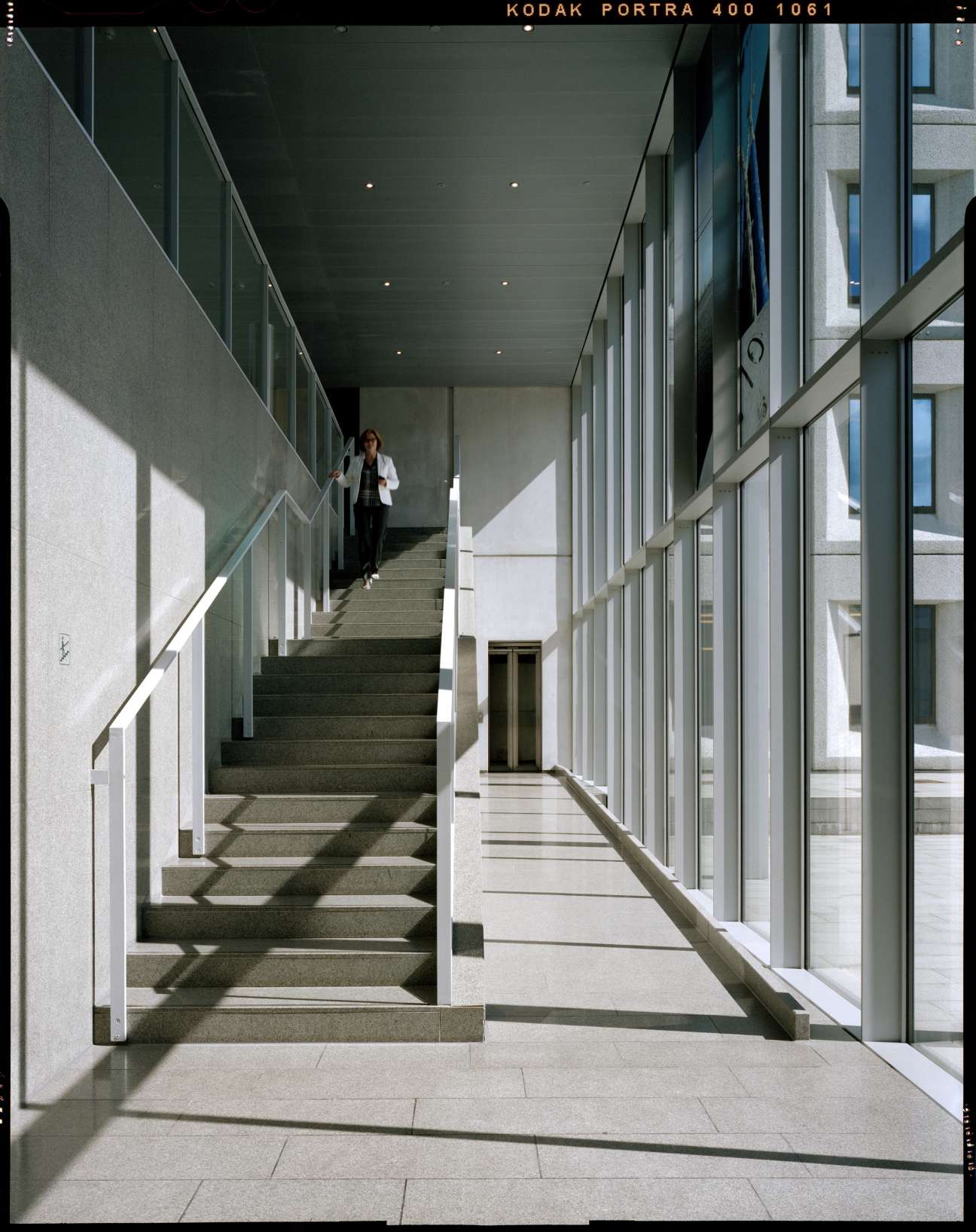 Modernist stairway with natural light from central courtyard, minimalist design with clean lines and glass railings.