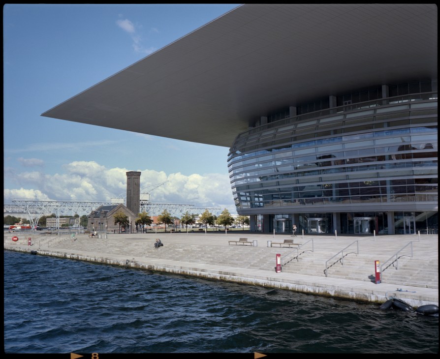 Copenhagen Opera House with curved glass facade and modern architecture overlooking waterfront plaza.