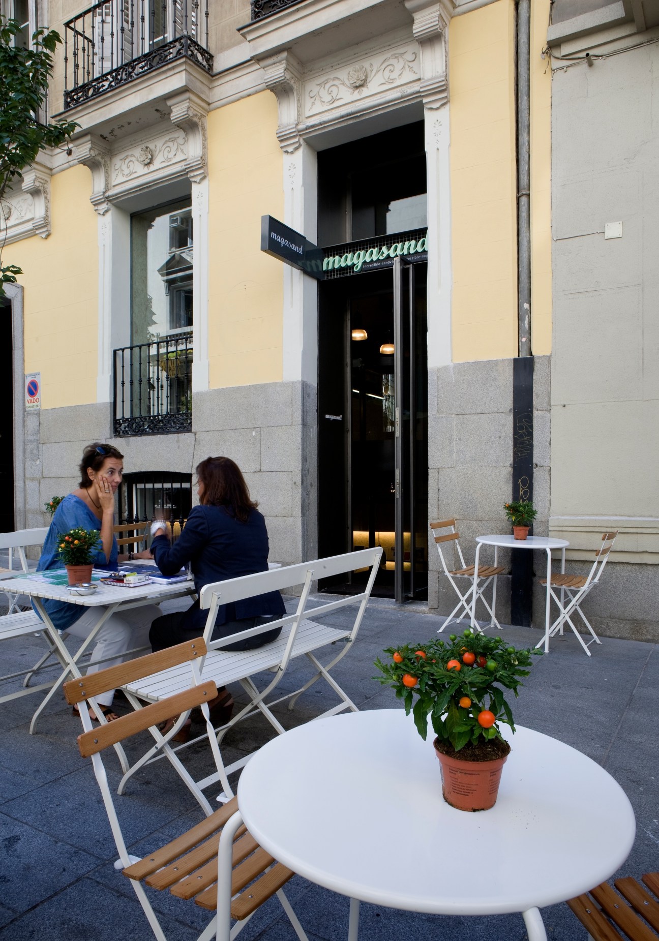 Magasand café exterior in Madrid with outdoor seating and signage on yellow building.