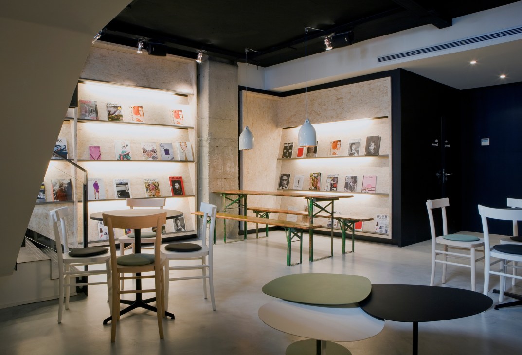 Interior of Magasand cafeteria in Madrid featuring illuminated shelving with magazines and books, modern furniture, and round tables.