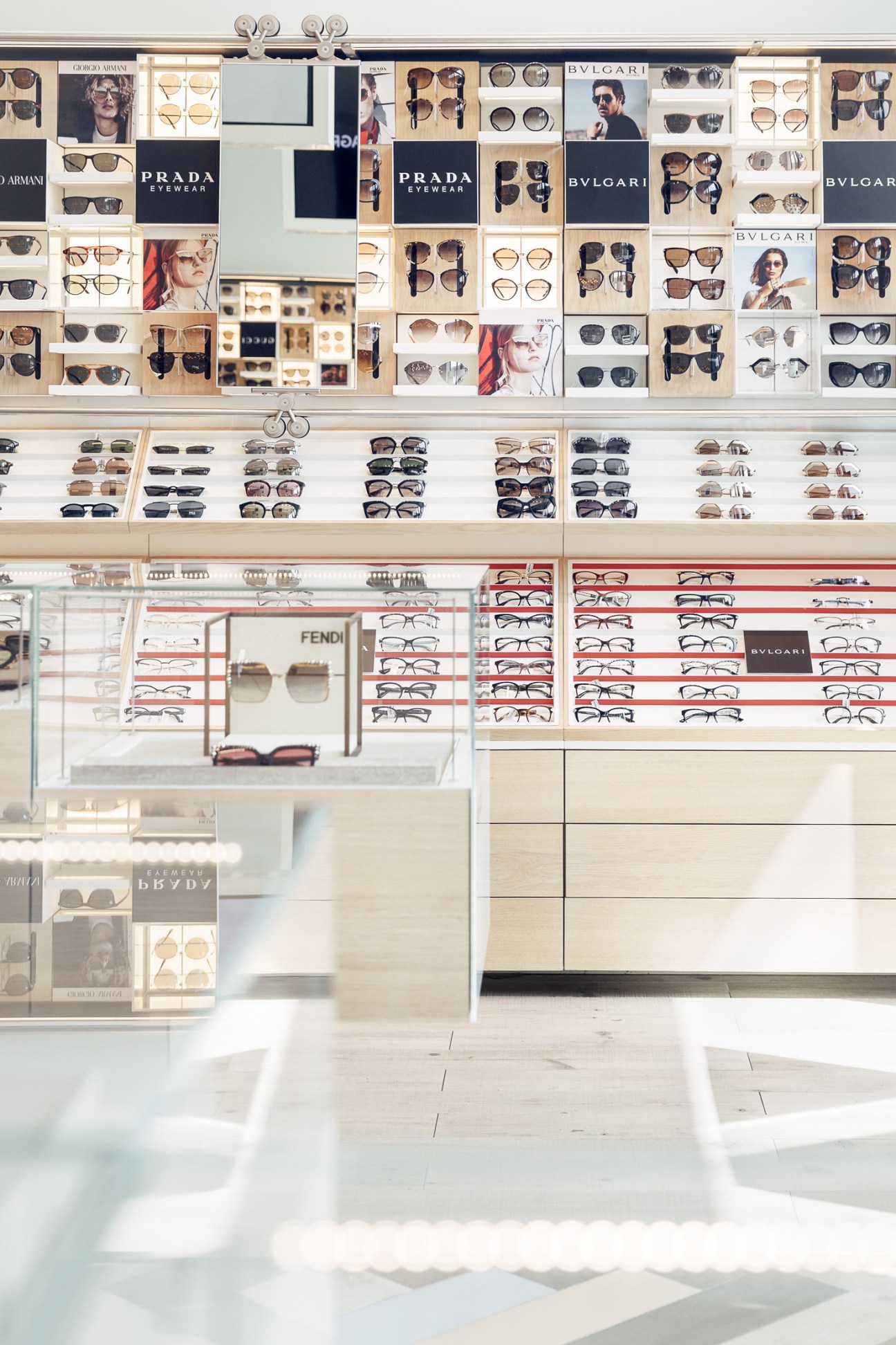 Interior of Magrabi eyewear shop displaying luxury sunglasses and spectacles from brands including Prada, Bulgari and Giorgio Armani on white shelving.
