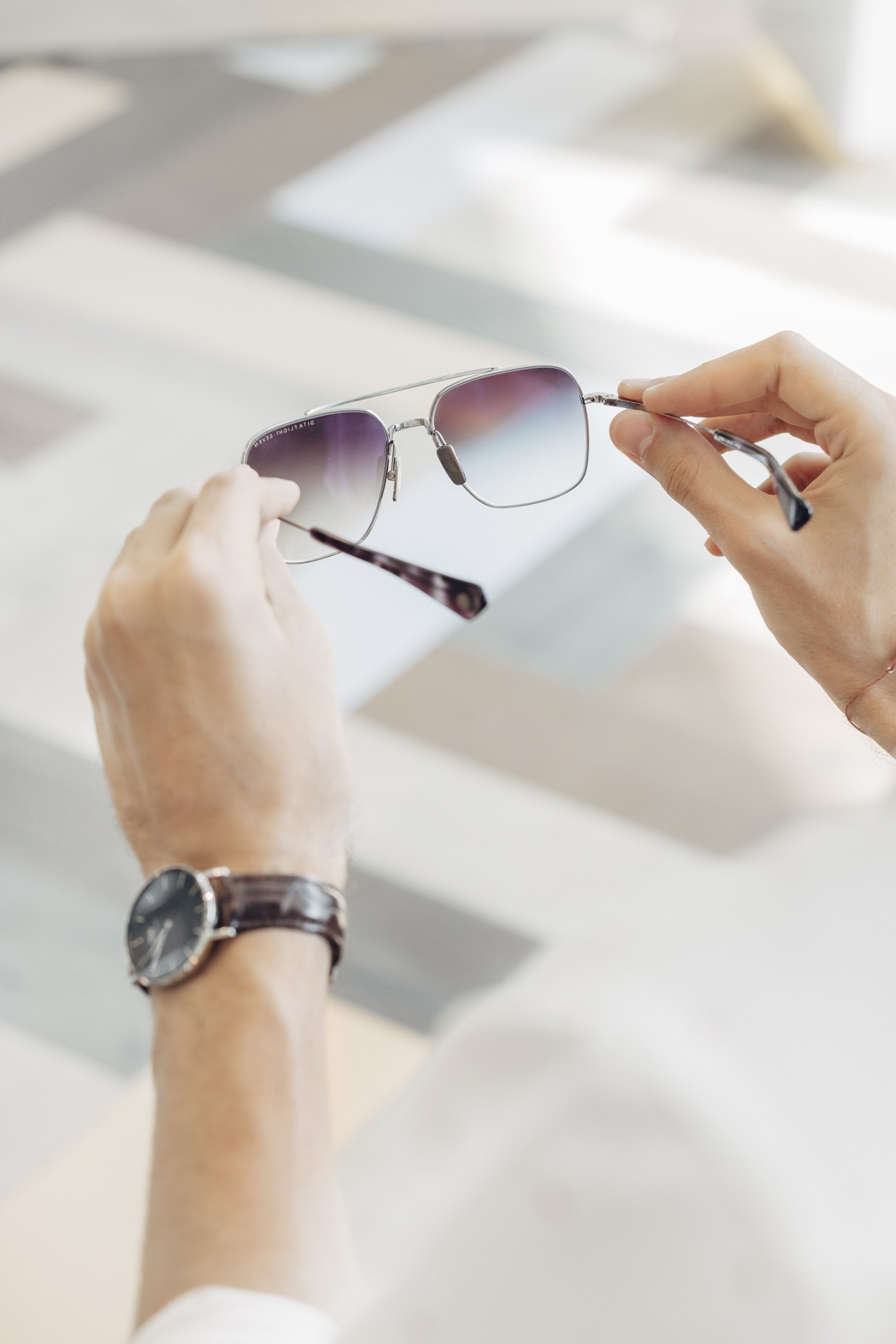 Person holding gradient-tinted sunglasses with metal frames against a bright background.