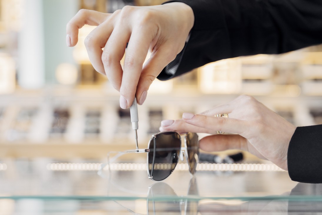 Optometrist making adjustments to a pair of sunglasses with a precision screwdriver tool.