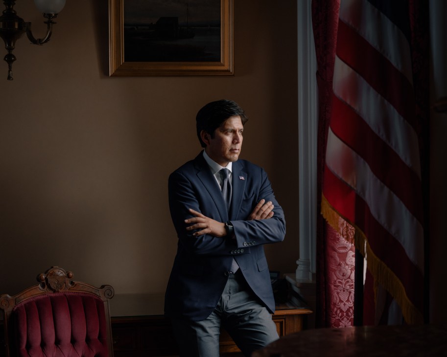 Senate president pro tempore Kevin de León stands with arms crossed in a formal government office next to an American flag.