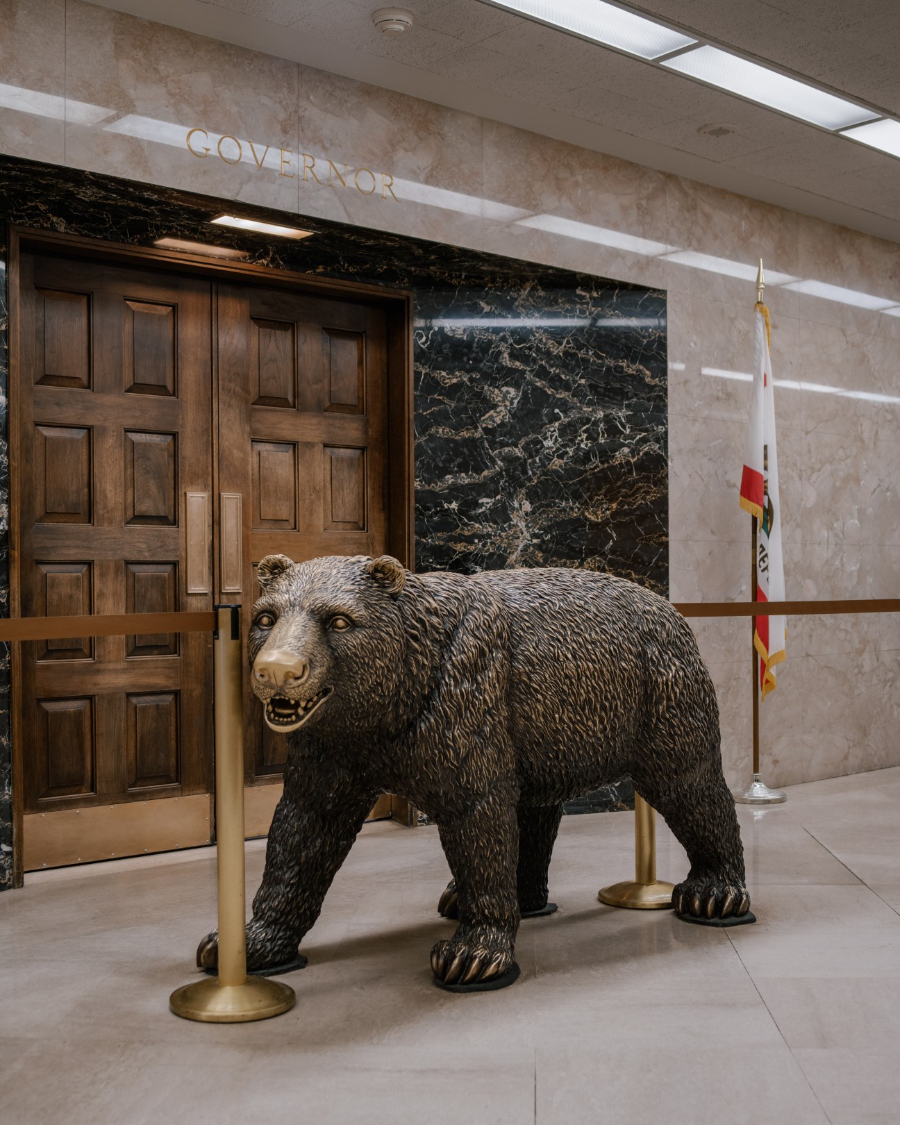 A bronze bear statue stands in Governor Jerry Brown's office entrance, flanked by wooden doors and a California state flag.