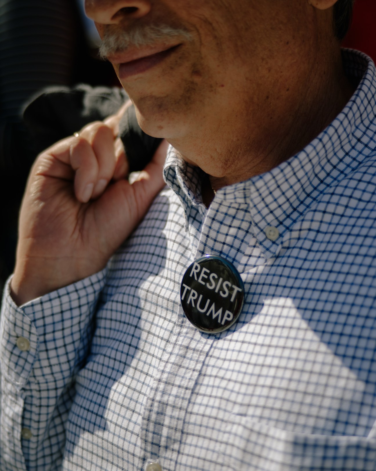 Man wearing blue checkered shirt with "Resist Trump" button at anti-Trump protest.