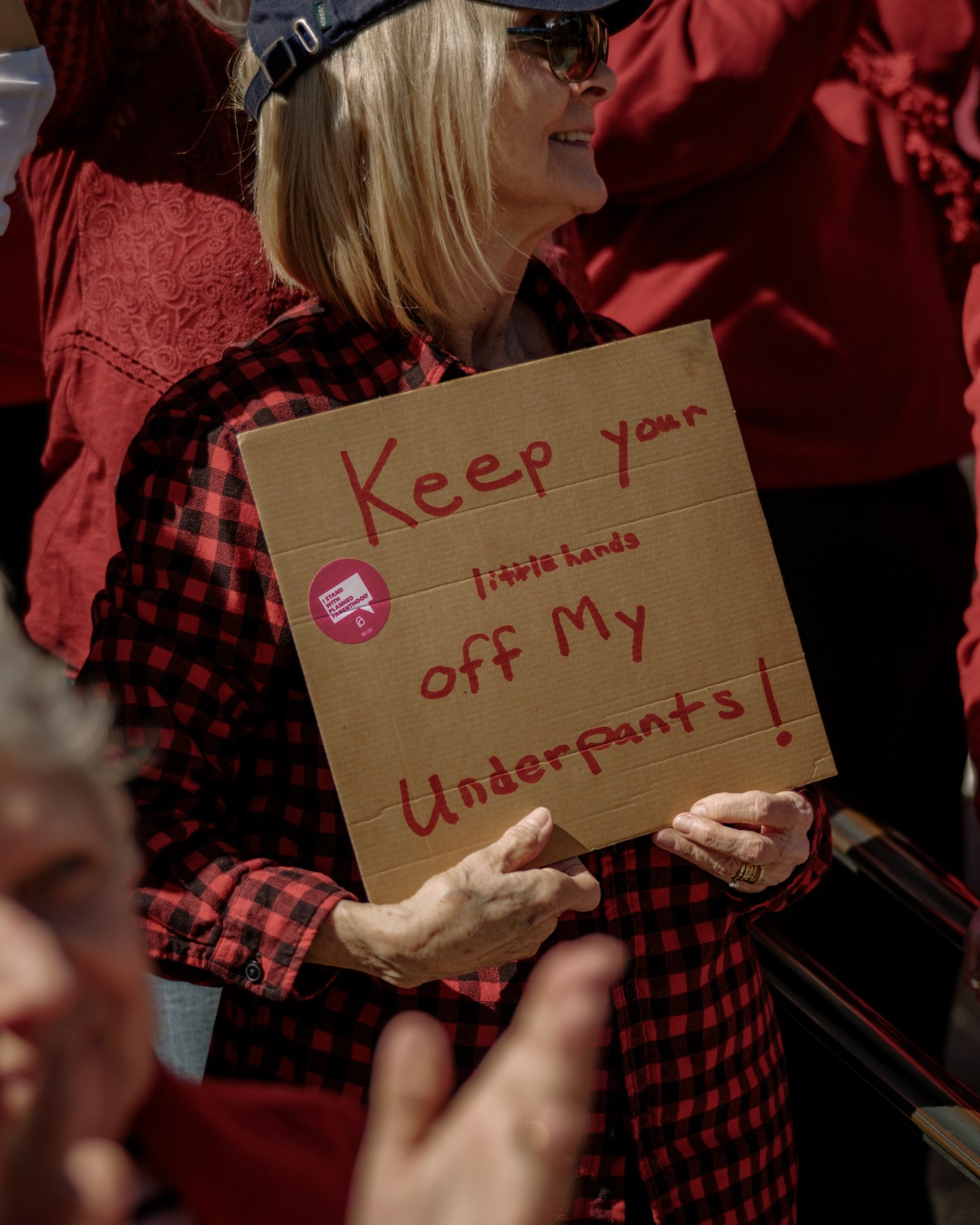 Woman holding cardboard protest sign reading "Keep your little minds off my Underpants!" at anti-Trump rally