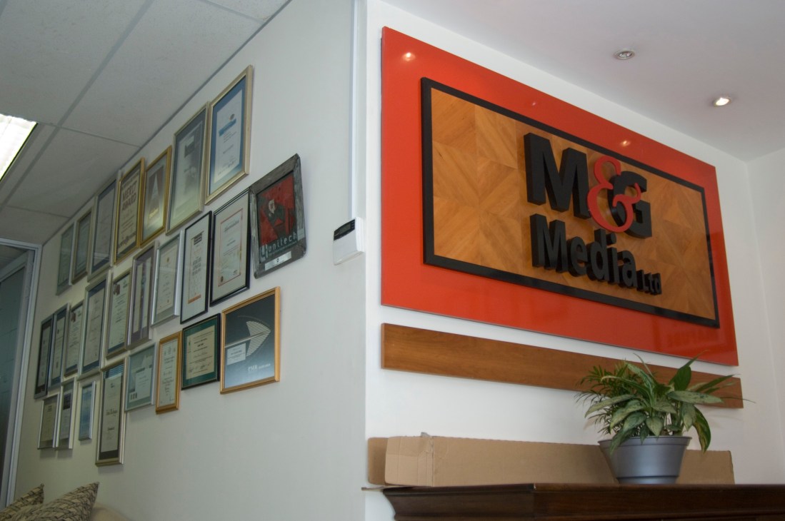 M&G Media's reception area with framed awards on the wall and the company logo on an orange sign.