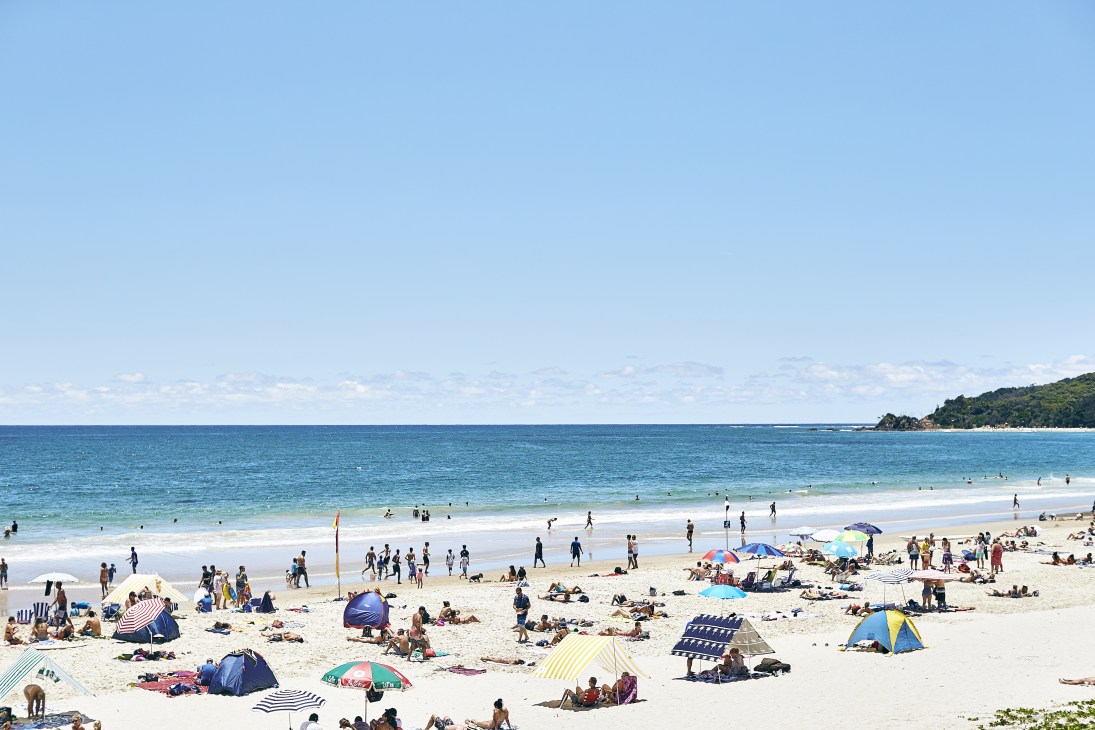 Crowded beach with swimmers, sunbathers and colorful umbrellas under clear blue sky
