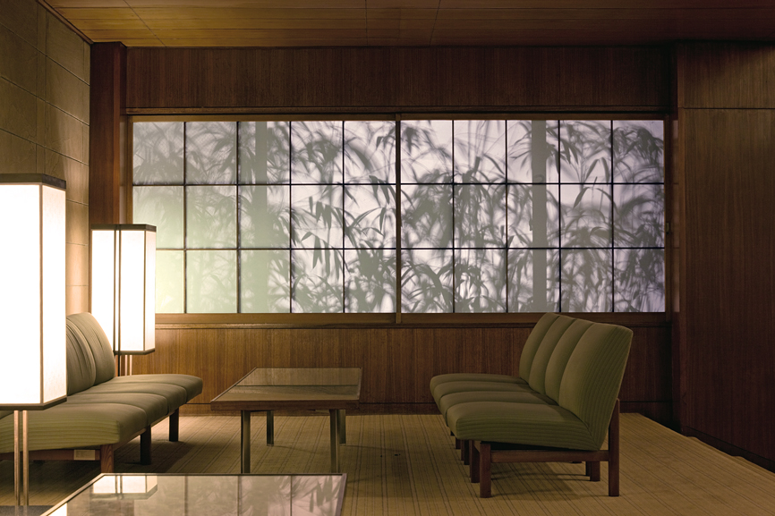 Hotel Okura lobby with green upholstered chairs, wooden paneling, and paper screens casting bamboo silhouettes.