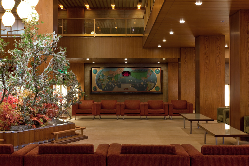 Hotel Okura's 1960s lobby featuring a Seiko world clock, wooden paneling, red seating, and seasonal floral arrangement.