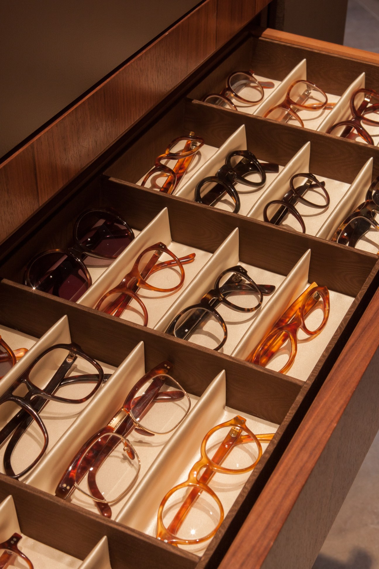 Handmade eyeglass frames in tortoiseshell, acetate, and horn displayed in a wooden drawer with compartments at Maison Bonnet.