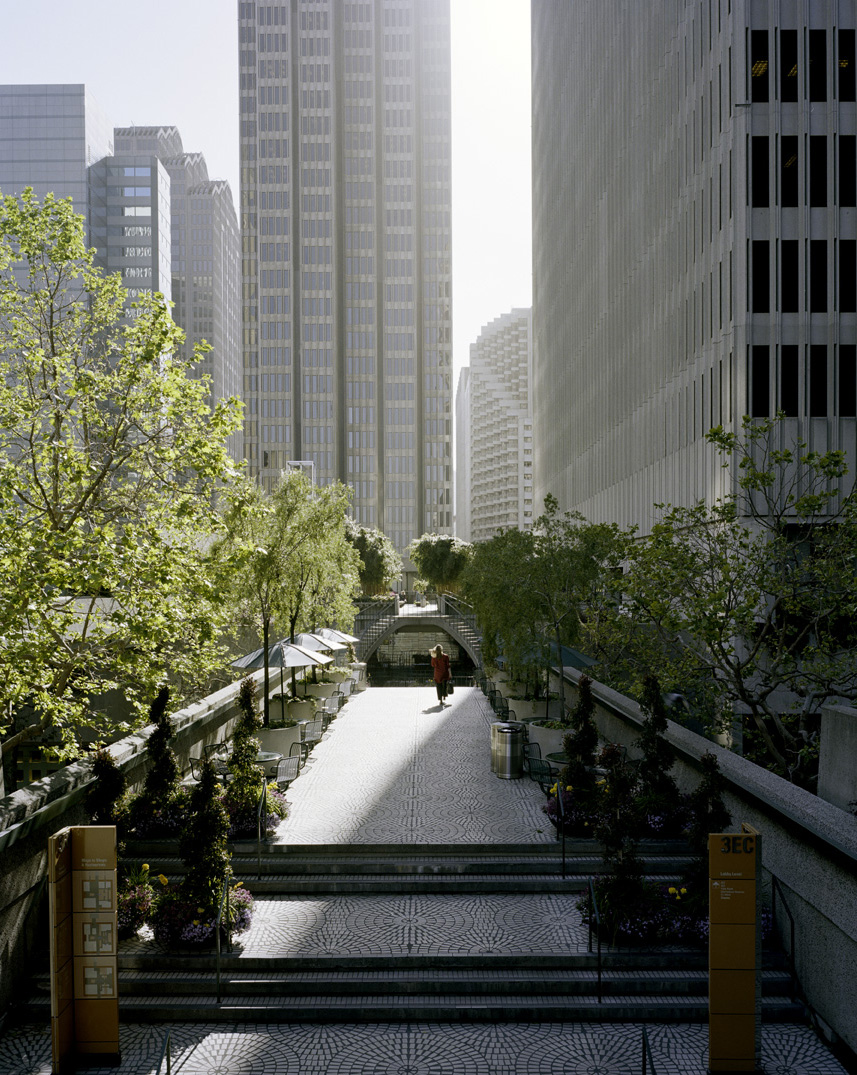 A pedestrian walkway lined with green trees between tall office buildings in San Francisco.