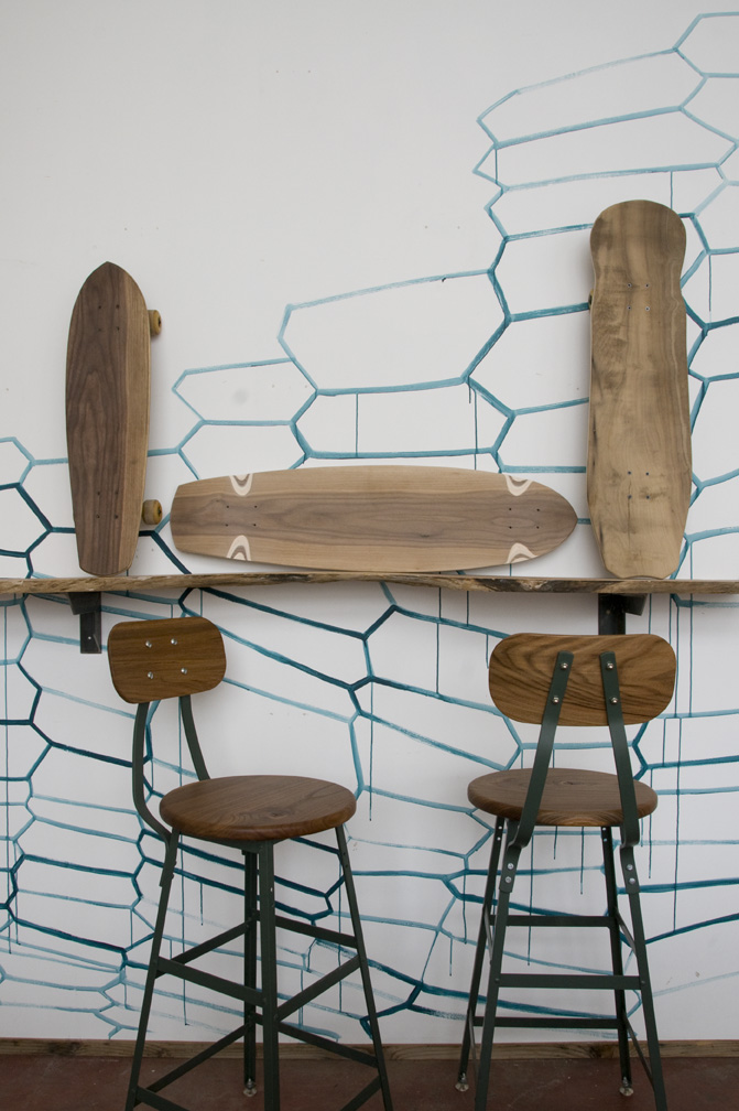 Woodshop showroom displaying wooden surfboards and bar stools with metal frames against a wall with blue hexagonal pattern.