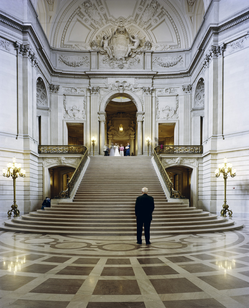 Interior of San Francisco City Hall with grand staircase, ornate ceiling, and classical columns.