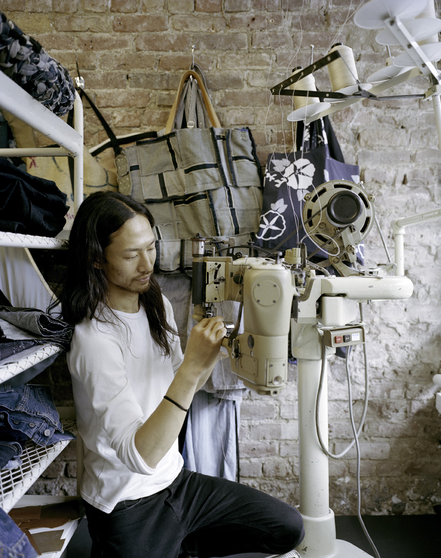 Worker sewing at MatoCreative workshop with fabrics and materials displayed on brick wall.