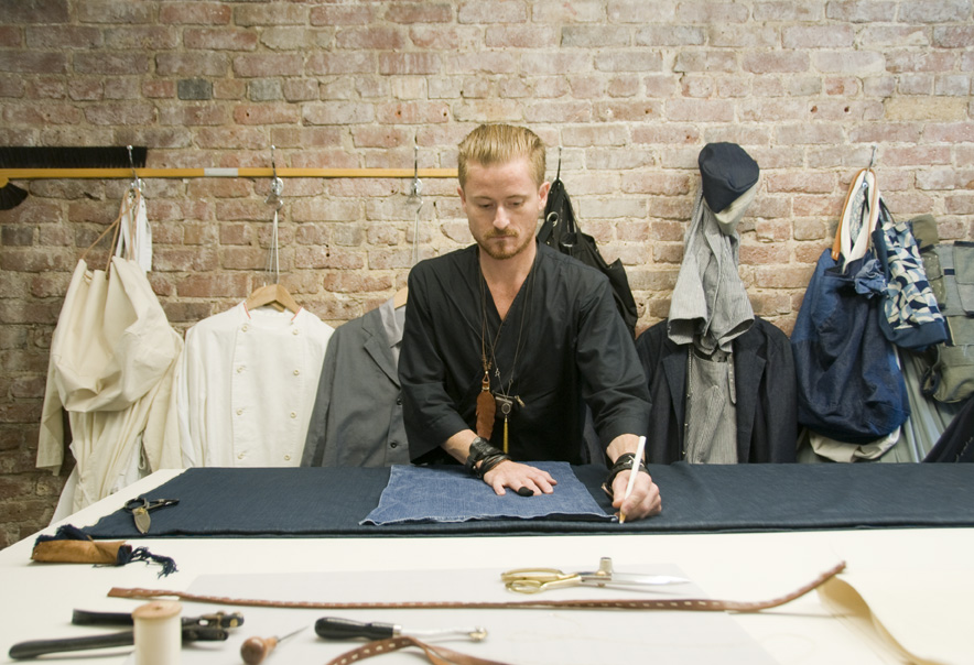 Matt Dick working at a table in his MatoCreative workshop surrounded by fabric and craft tools.