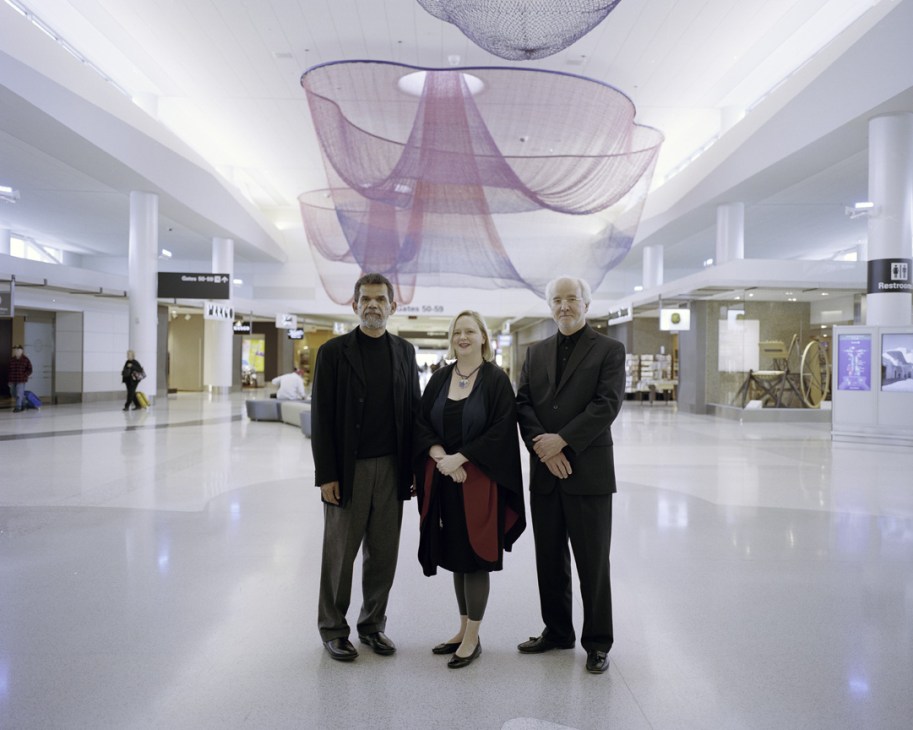 Three professionals standing in a modern airport terminal with purple sculptural art installation overhead.