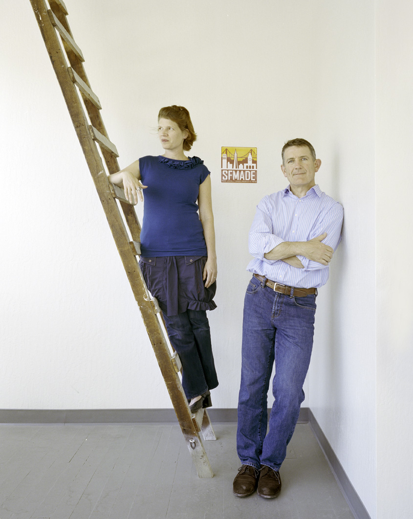 Kate Sofis and Mark Dwight, founders of SFMade, stand against a white wall with a wooden ladder and SFMade logo visible.