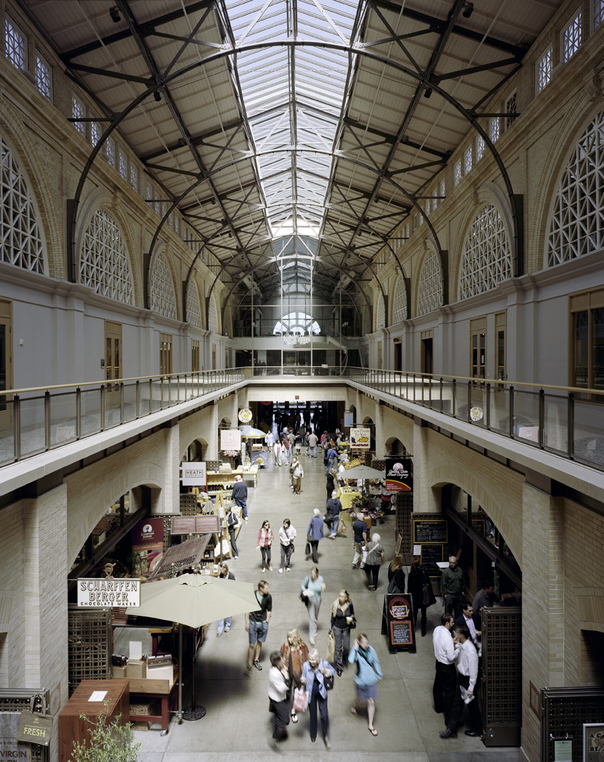 Interior view of San Francisco Ferry Terminal with vaulted glass ceiling, two levels of shops and vendors, and people browsing.