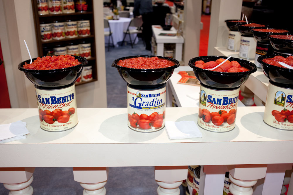 Sample tomato sauces from San Benito displayed in black bowls on cans at the International Pizza Expo.