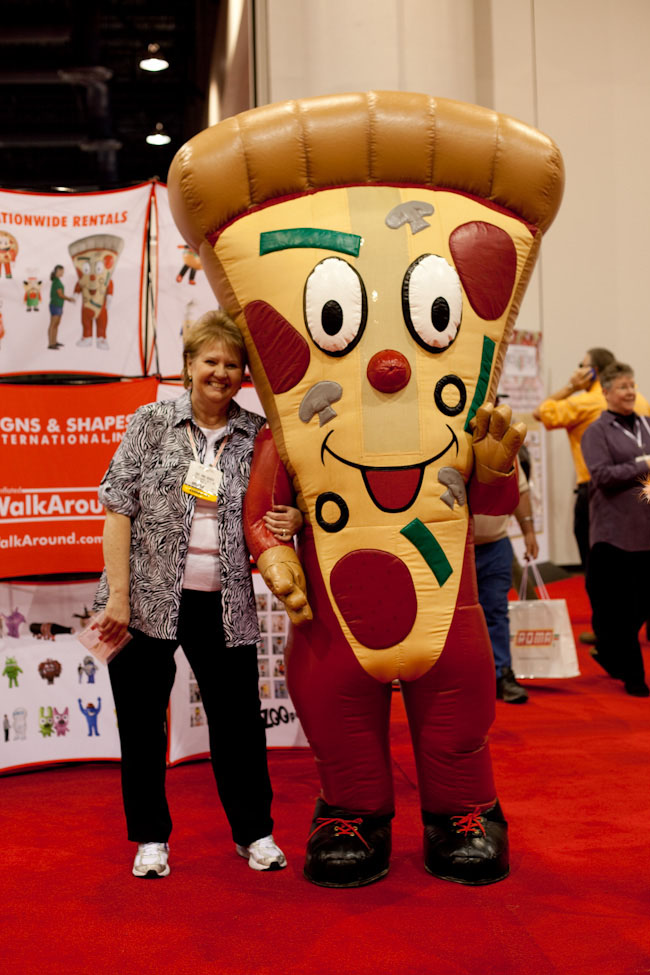 A woman poses with a large inflatable pizza slice mascot at the International Pizza Expo.