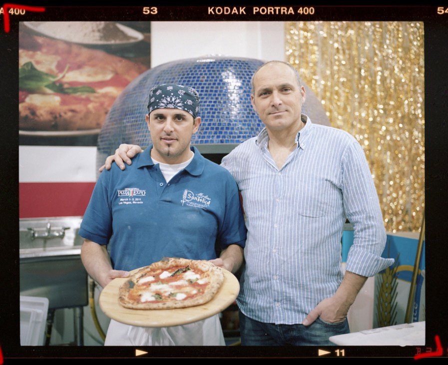 Dino Santonicola, a Neapolitan pizzeria owner, holds a freshly made pizza beside another man at the International Pizza Expo in Las Vegas.