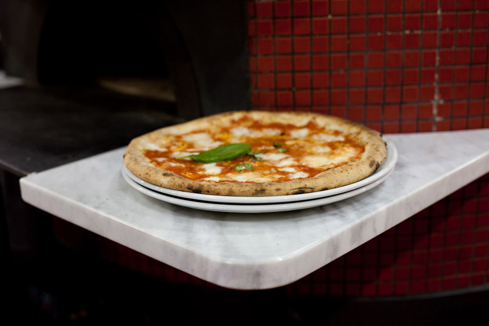 Freshly cooked Neapolitan pizza with tomato sauce, mozzarella and basil on a white plate.