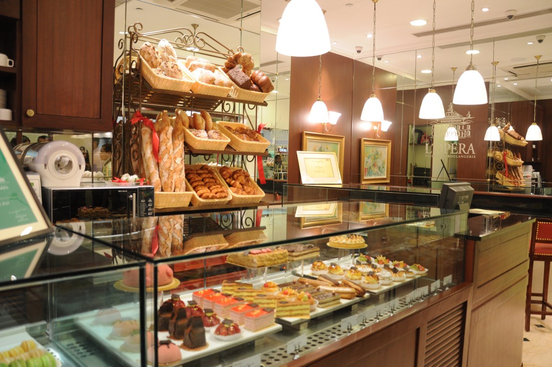L'Opera French patisserie interior with display cases of baked goods and pastries under pendant lighting.