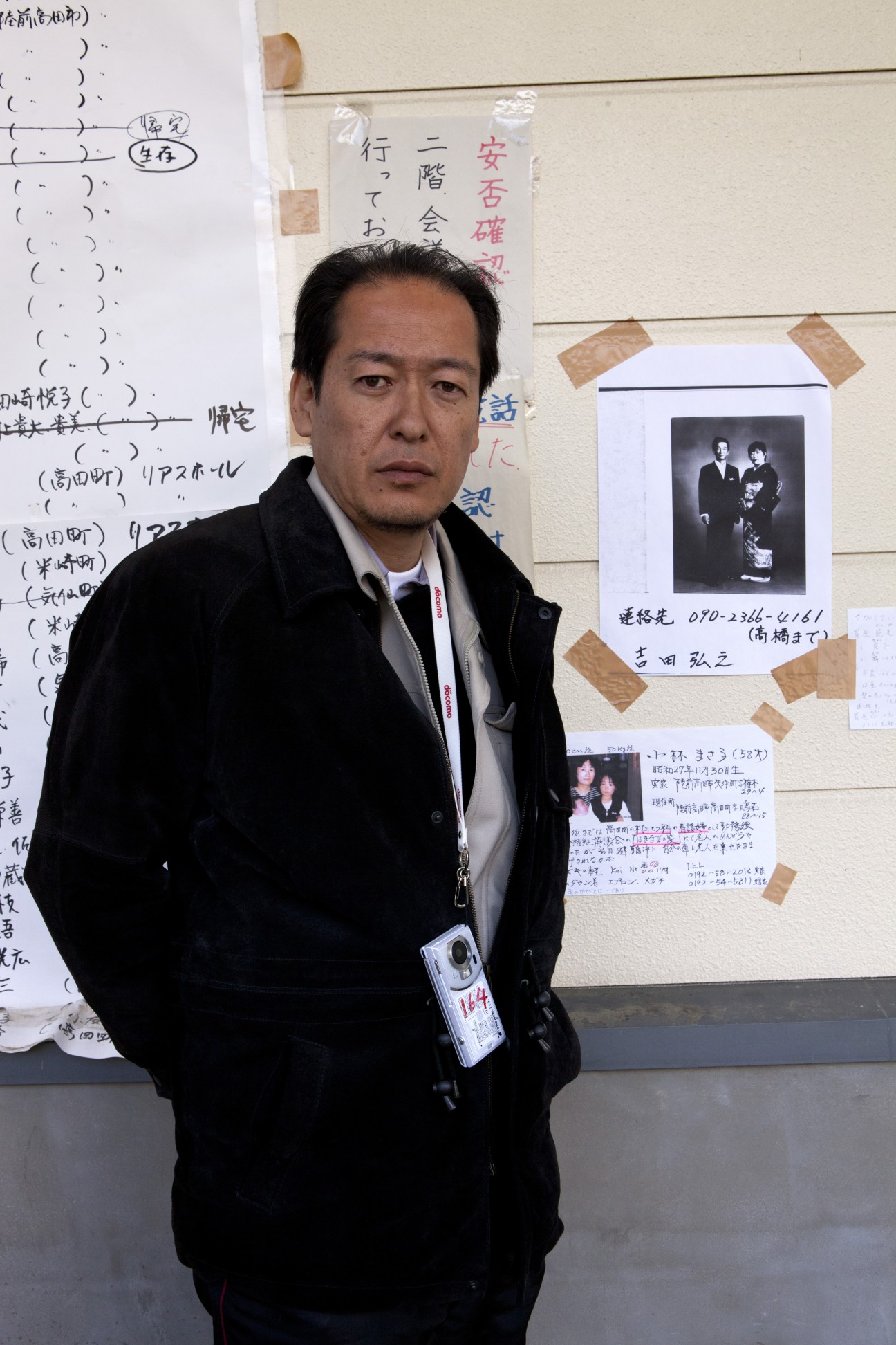 Futoshi Toba, mayor of Rikuzen-Takata, standing in front of a wall with Japanese notes and photographs.