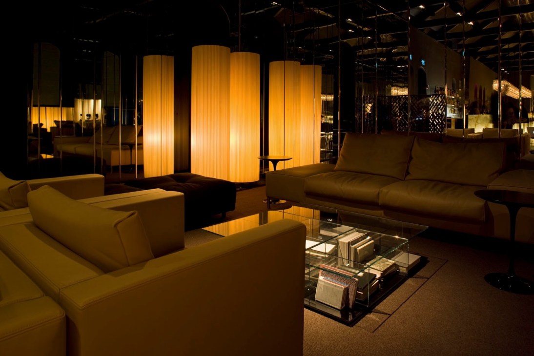 Modern hotel lounge with illuminated golden pendant lamps, cream seating, and minimalist furnishings.