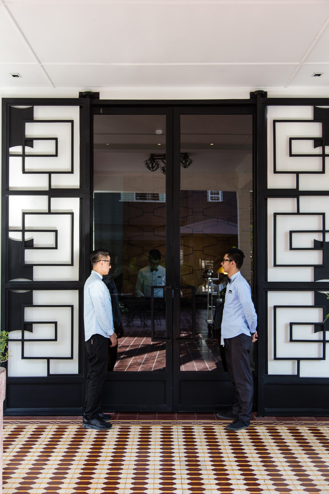Two men stand facing each other outside The Henry Hotel's lobby entrance with geometric patterned doors and decorative floor tiles.