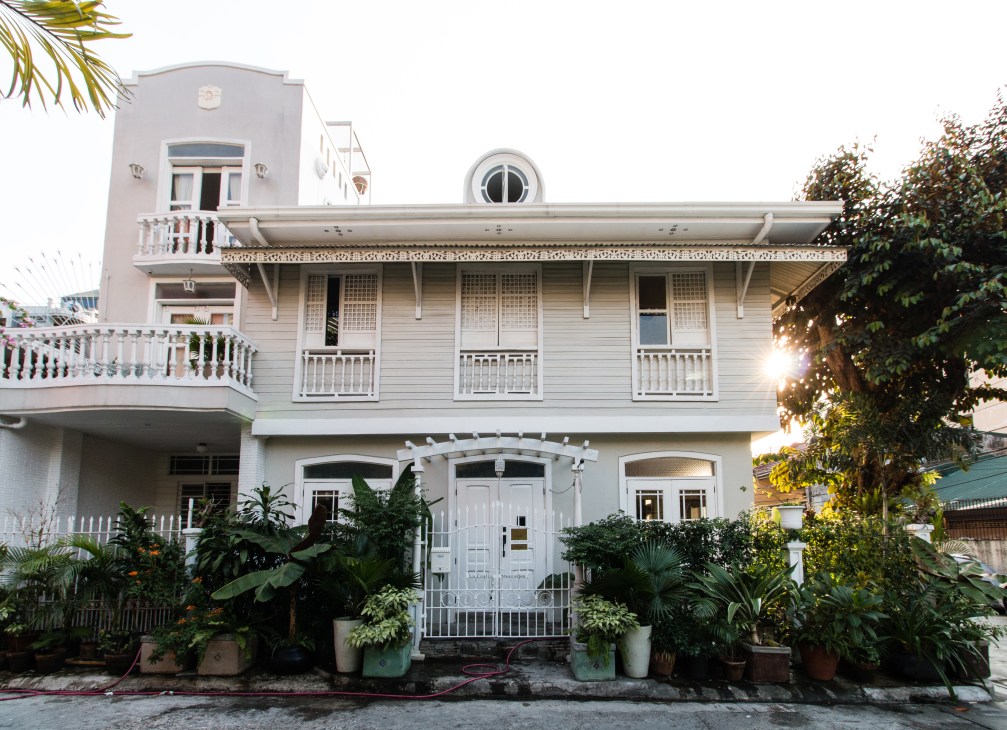 White heritage wooden building with balconies and shutters, surrounded by potted plants in Manila's Makati City.