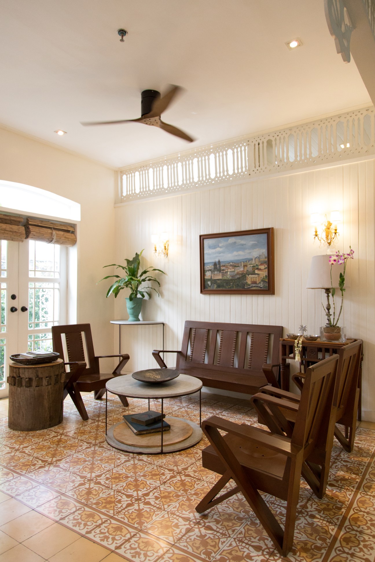 Light-filled common area with wooden furniture, potted plants, framed artwork, and decorative tiles at La Casita Mercedes in Manila.