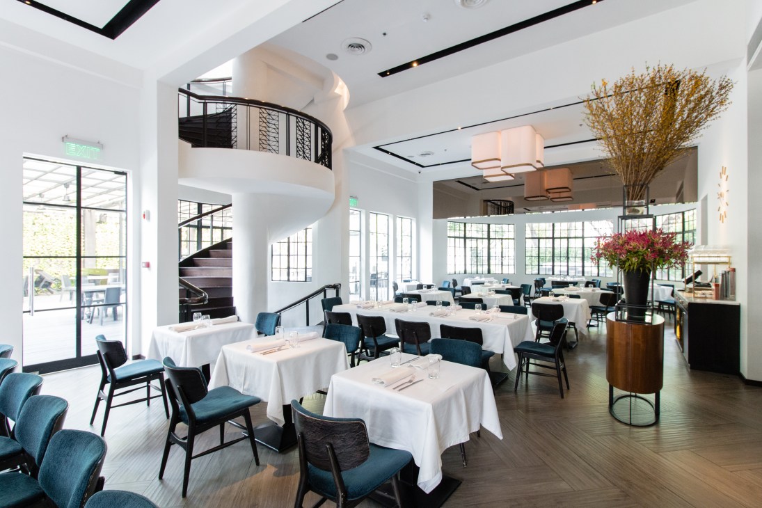 Modern restaurant interior with white tablecloths, blue chairs, spiral staircase and large windows at Blackbird in Manila.
