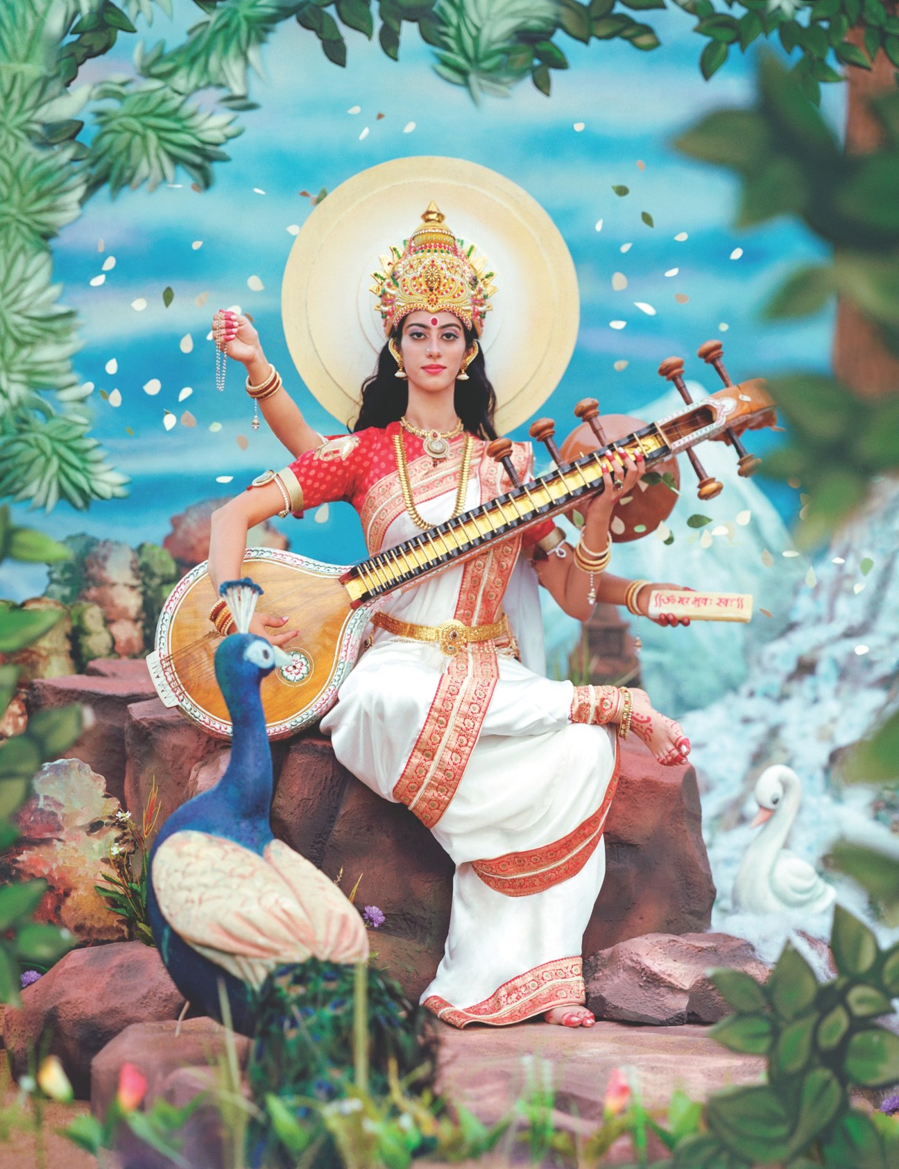 Photograph of Hindu goddess Saraswati figure with ornate headdress, holding a stringed instrument, with peacock and flowering plants.