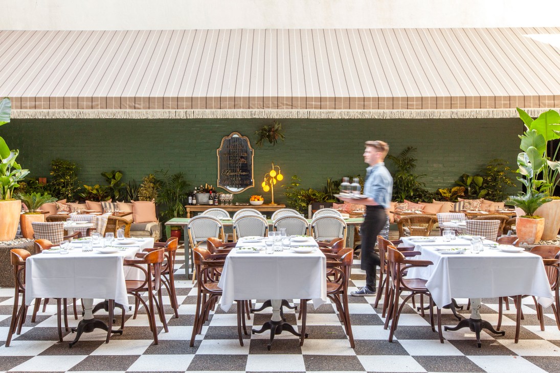 Outdoor restaurant patio at Mardi with white-clothed tables, woven chairs, and green wall with potted plants.