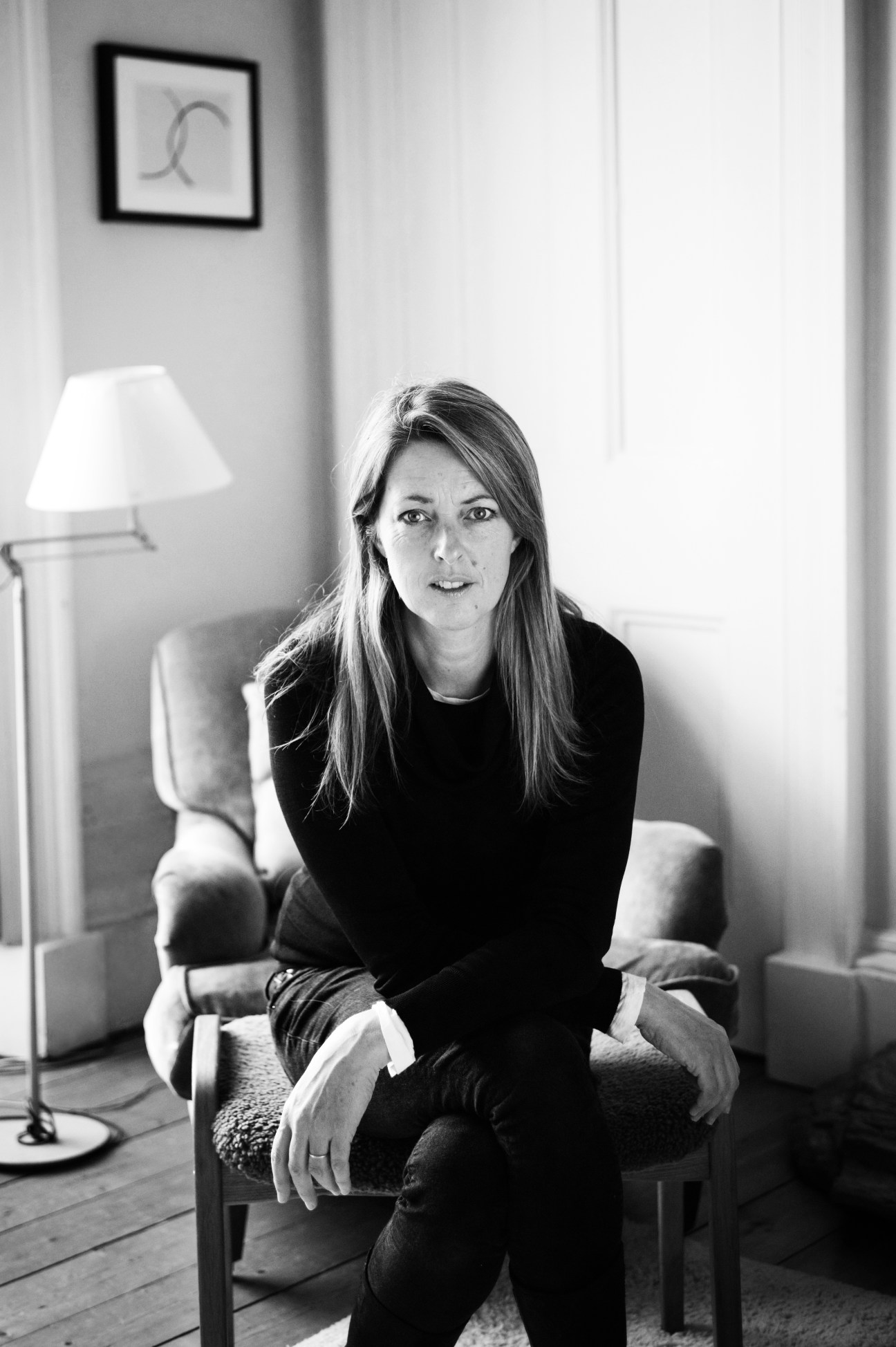 Margot Wilson, executive editor of The Arts Journal, sitting in a chair in a minimalist interior.