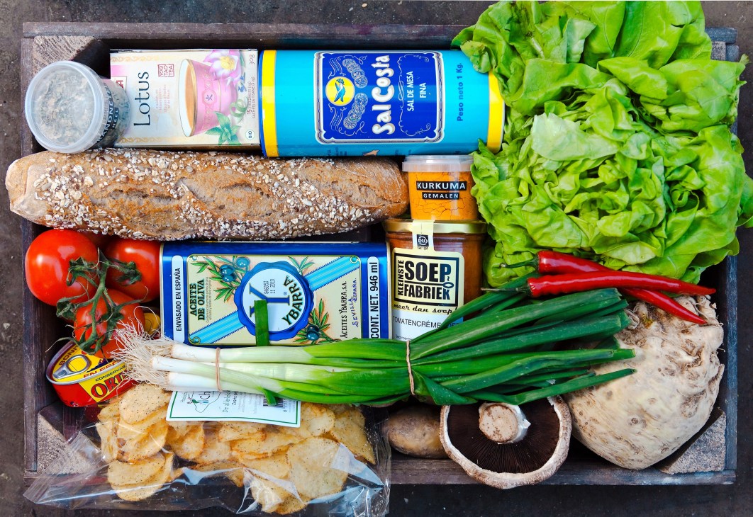 Overhead view of Marqt supermarket products including bread, fresh vegetables, local brands, and groceries arranged on dark surface.