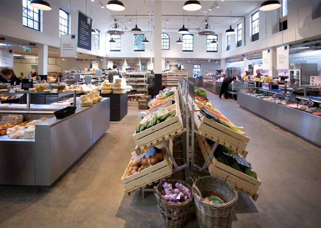 Interior of Marqt supermarket in Amsterdam with produce displays, wooden crates, and customers shopping.