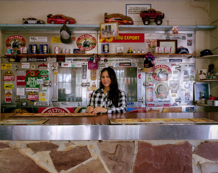 A woman in a checkered shirt stands at a counter decorated with toy cars, beer signs and memorabilia at the Kumarina roadhouse.