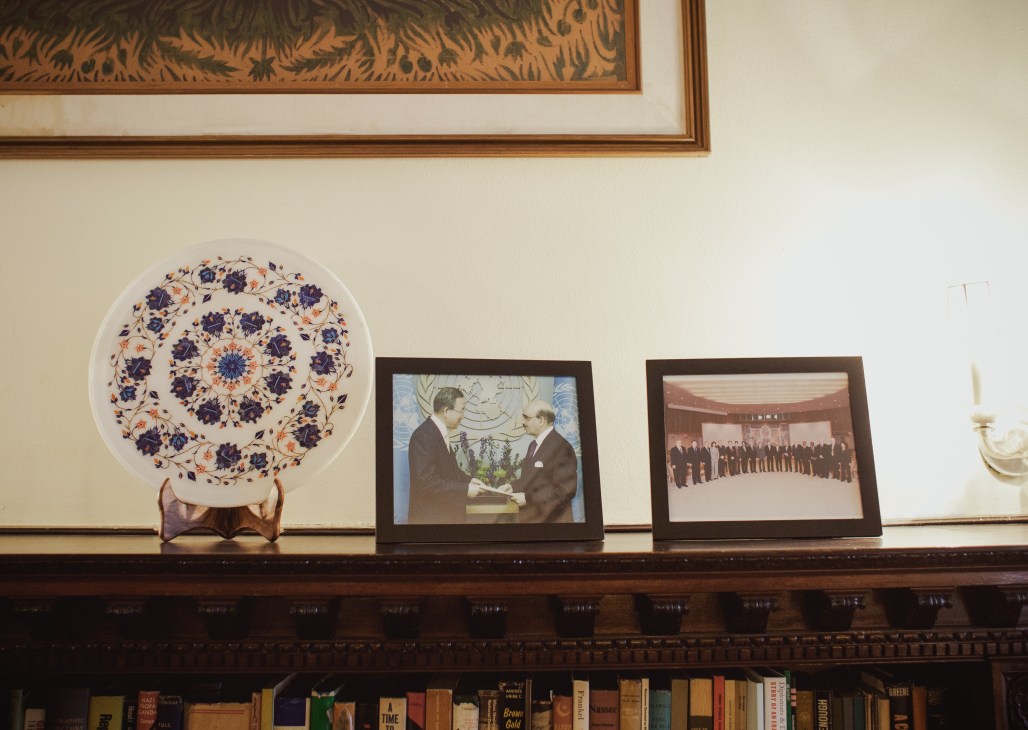 Mantelpiece display with decorative plate, framed photographs, and books at Pakistan's UN mission residence.