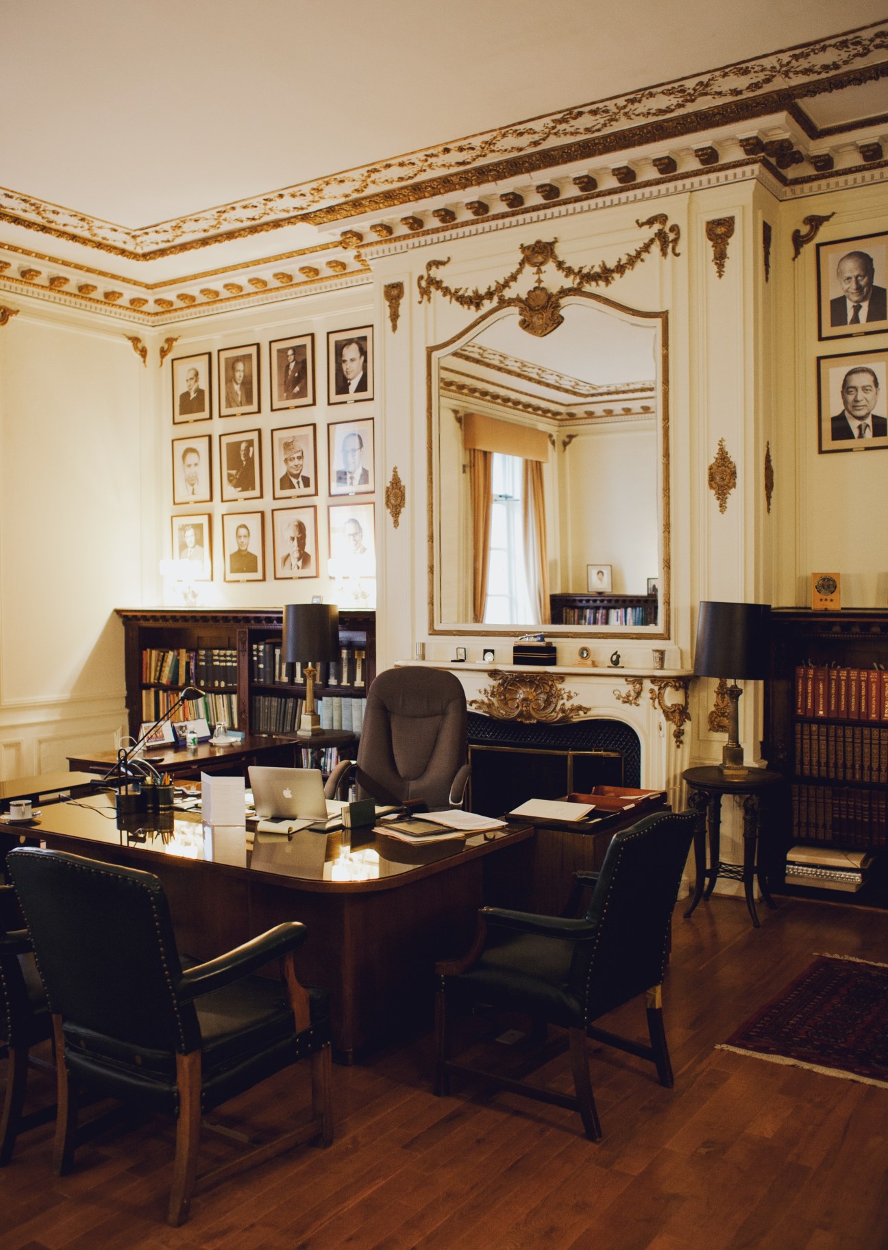 Elegant diplomatic office with ornate gold ceiling, portrait gallery, desk and bookshelves.
