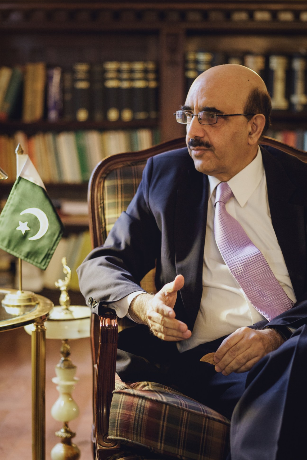 Masood Khan, Pakistan's permanent representative to the UN, sits in his office with bookshelves behind him and a Pakistani flag on his desk.