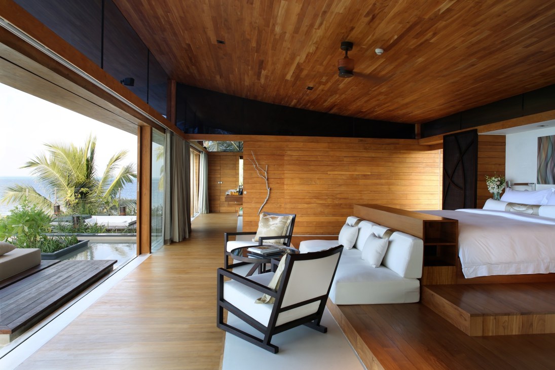 Luxury bedroom interior with teak wood finishes, white bedding, and ocean views at Coco Privé Maldives.