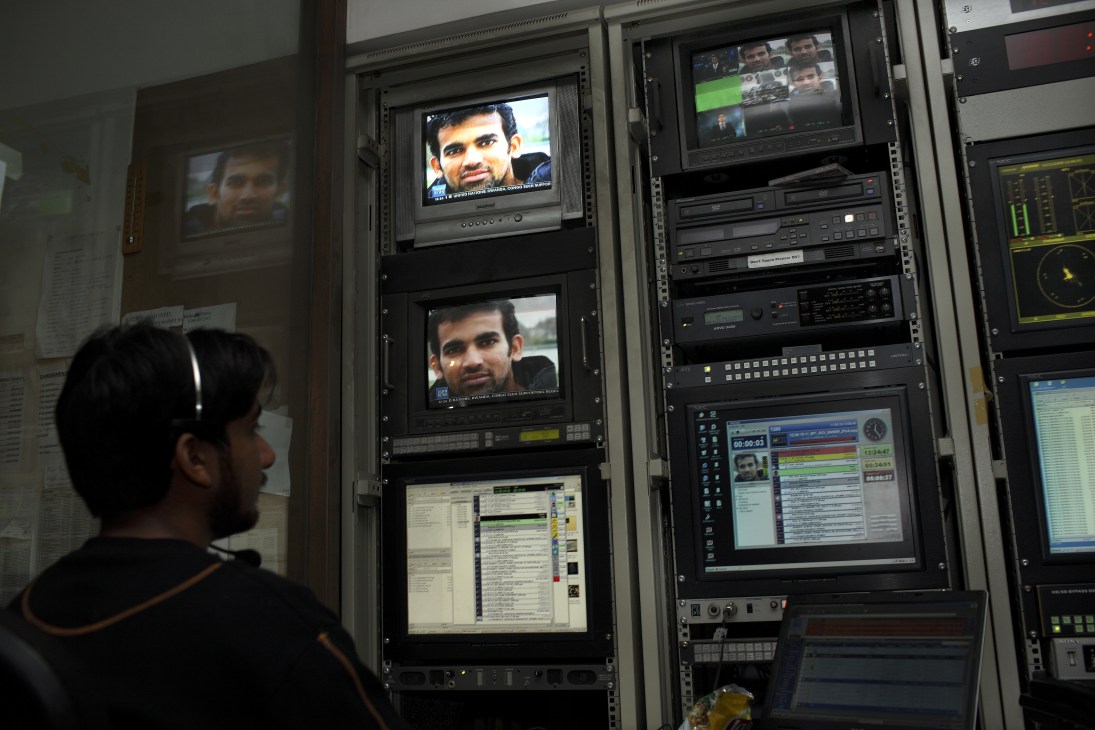 A technician monitors multiple screens displaying news content in a television master control room.