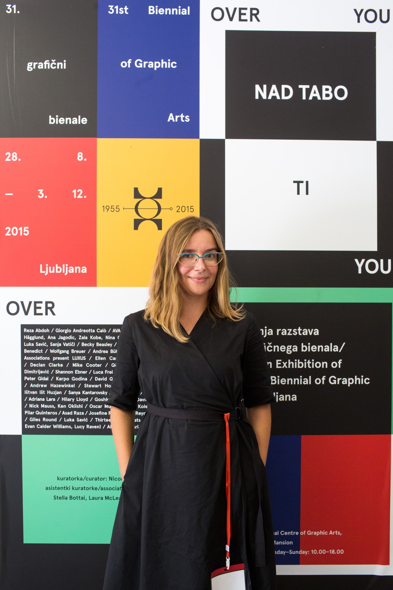 Graphic artist Mina Fina stands in front of a colorful poster display for Ljubljana's 31st Biennial of Graphic Arts.